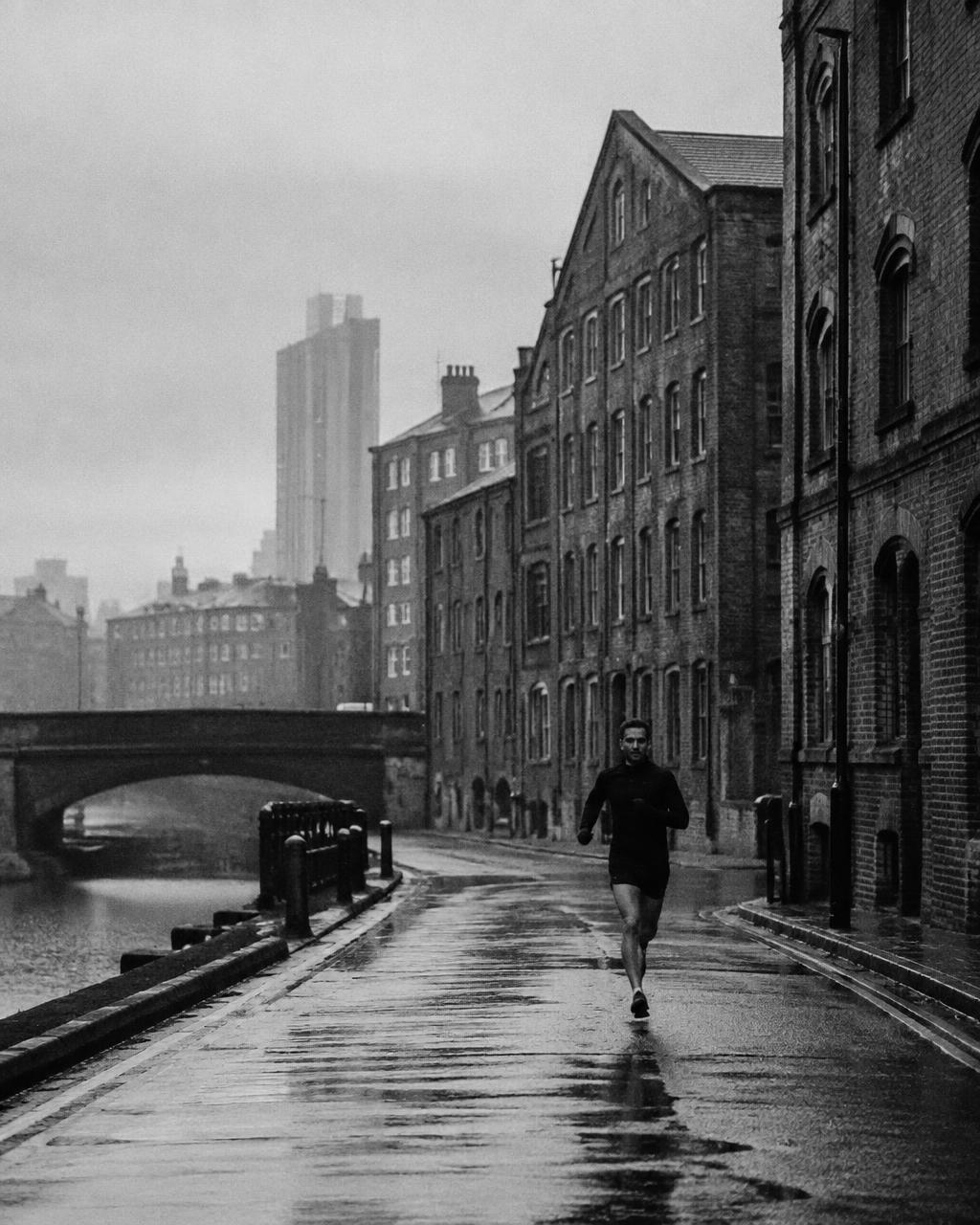 Runner on a wet street between red-brick mills