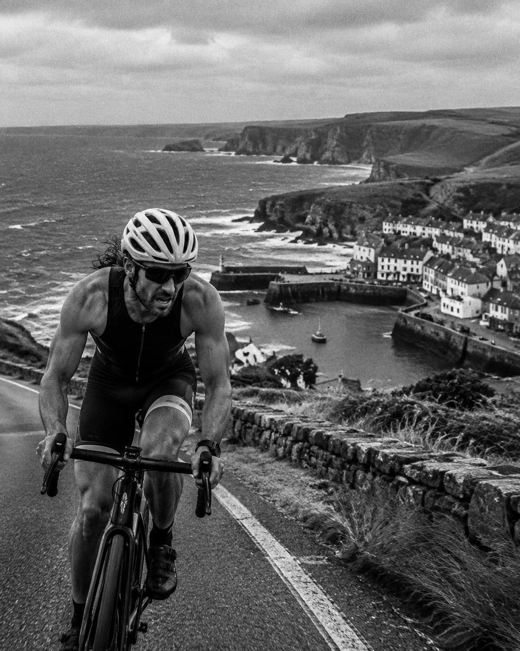 Triathlete cycling a coastal road above a harbour